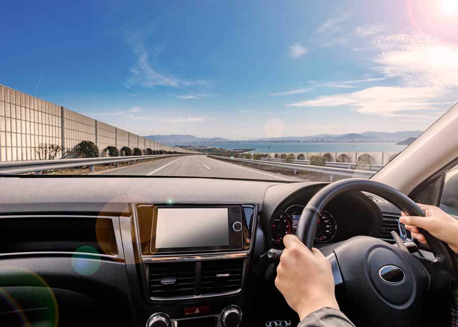 Car windscreen, hands holding steering wheel, blue sky and beach