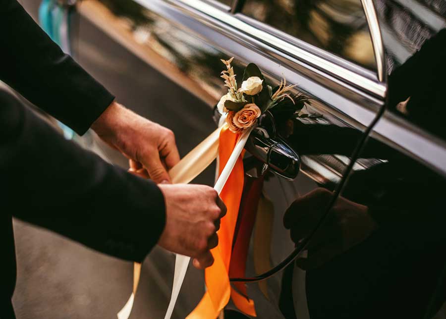 Hands tying ribbons and flowers around door handles, black polished car